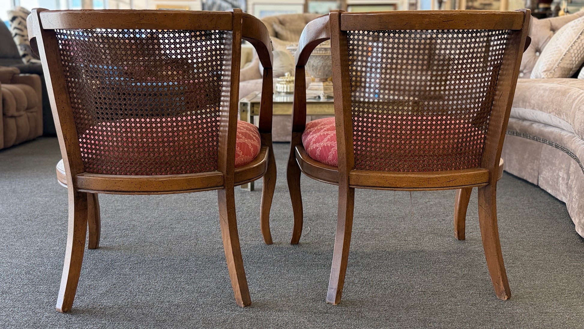 Set of two wooden armchairs featuring woven cane backrests, curved wooden arms, and red upholstered seats with a light geometric pattern.