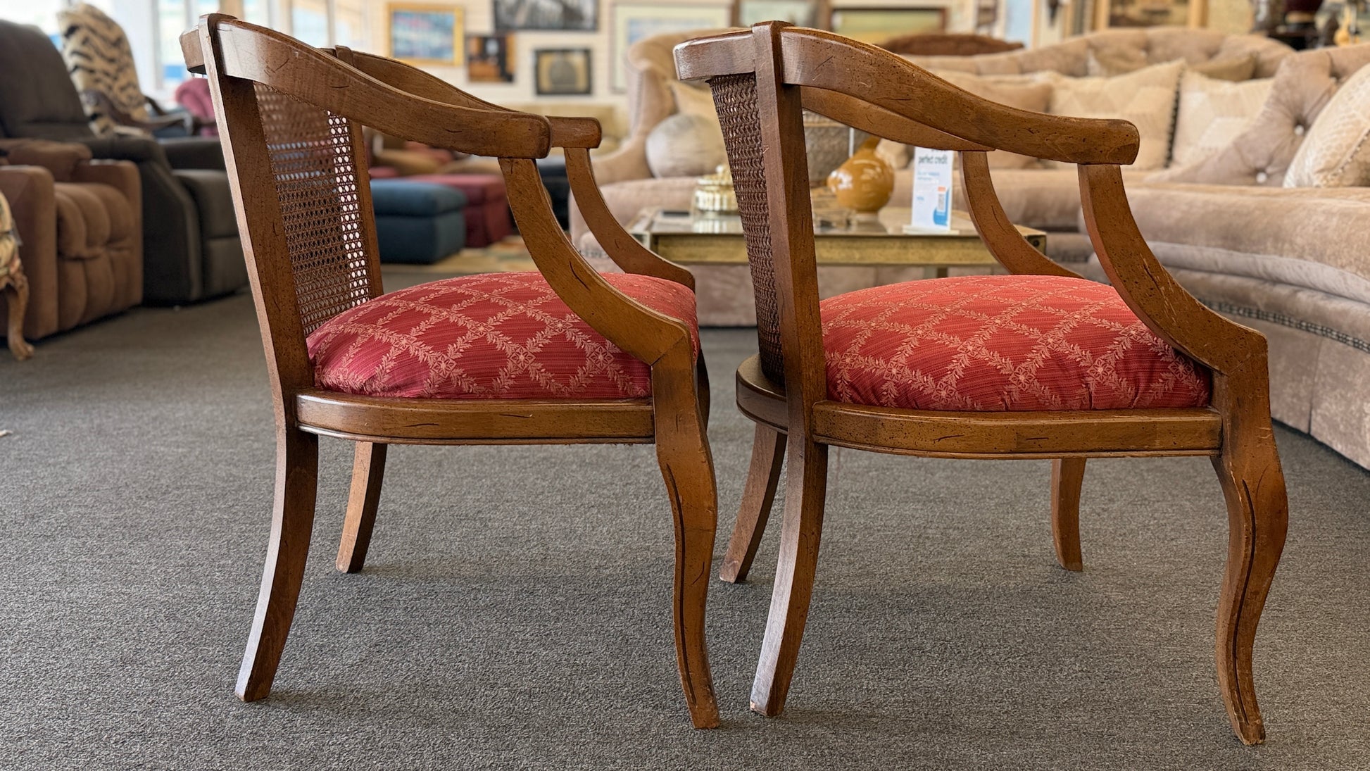 Set of two wooden armchairs featuring woven cane backrests, curved wooden arms, and red upholstered seats with a light geometric pattern.