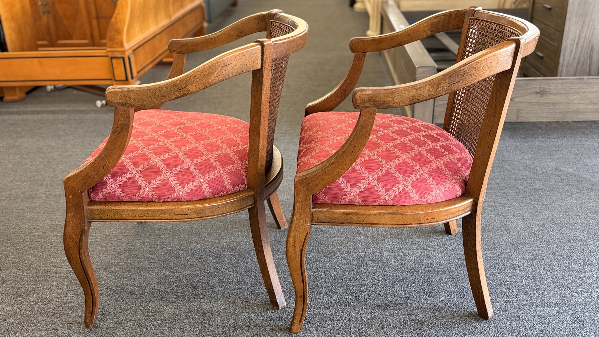 Set of two wooden armchairs featuring woven cane backrests, curved wooden arms, and red upholstered seats with a light geometric pattern.