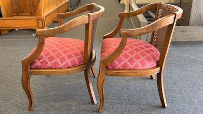 Set of two wooden armchairs featuring woven cane backrests, curved wooden arms, and red upholstered seats with a light geometric pattern.