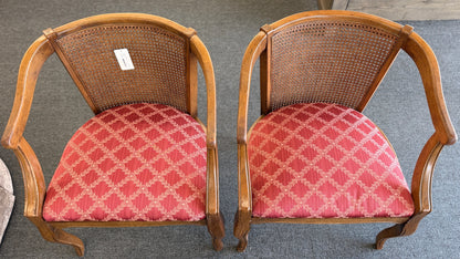 Set of two wooden armchairs featuring woven cane backrests, curved wooden arms, and red upholstered seats with a light geometric pattern.