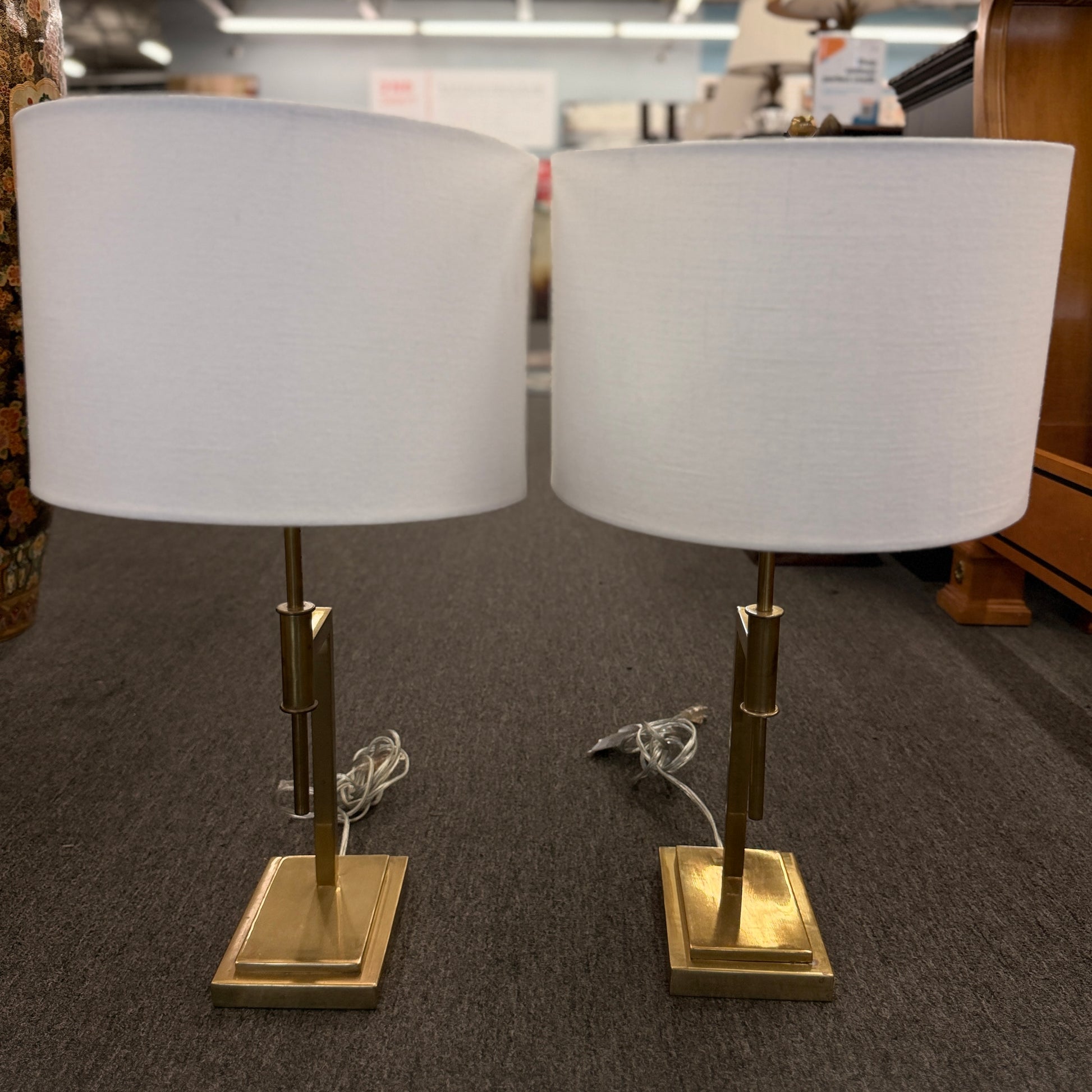 Matching pair of contemporary brass table lamps featuring stepped rectangular bases, angular geometric stems, and white fabric drum shades.