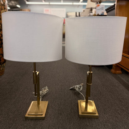 Matching pair of contemporary brass table lamps featuring stepped rectangular bases, angular geometric stems, and white fabric drum shades.