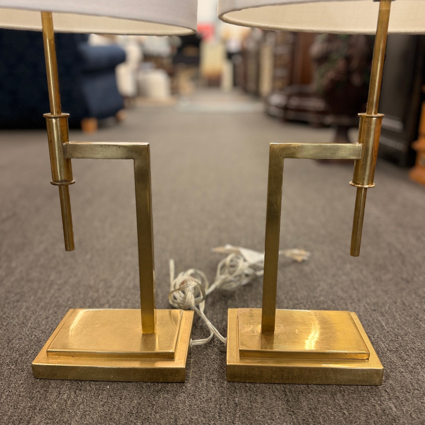 Matching pair of contemporary brass table lamps featuring stepped rectangular bases, angular geometric stems, and white fabric drum shades.