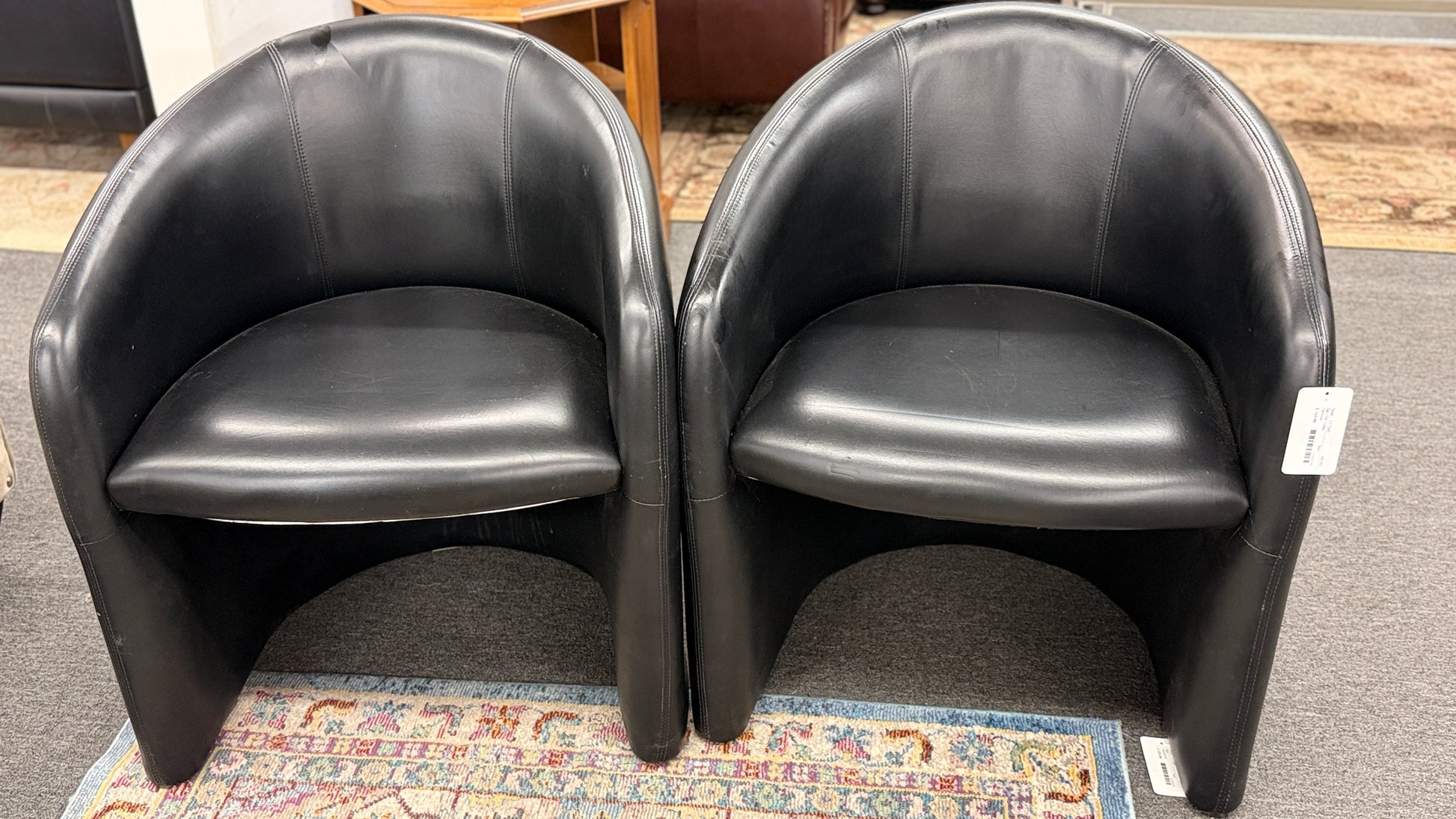 Set of two modern black barrel accent chairs featuring wraparound curved backs, thick integrated seat cushions, and a clean contemporary design.