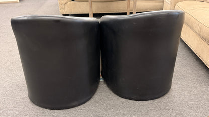 Set of two modern black barrel accent chairs featuring wraparound curved backs, thick integrated seat cushions, and a clean contemporary design.