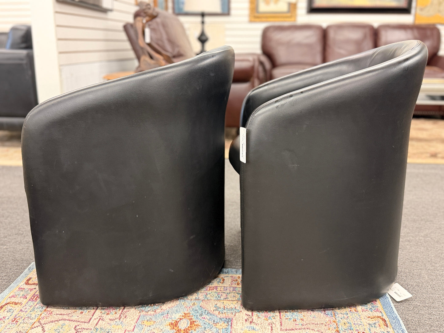 Set of two modern black barrel accent chairs featuring wraparound curved backs, thick integrated seat cushions, and a clean contemporary design.