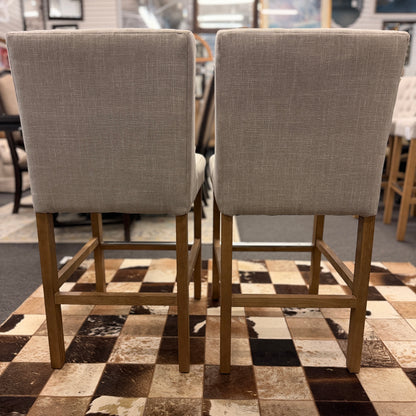 Set of two upholstered bar stools featuring wood and metal construction with comfortable fabric seats for kitchen islands or home bars.
