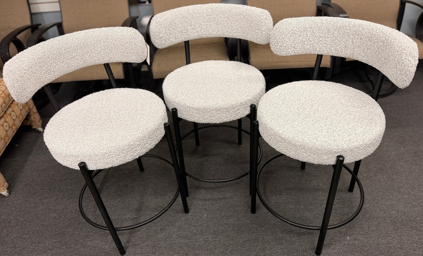 Set of three modern bar stools featuring textured white upholstered seats and curved backrests with sleek black metal frames and built-in footrests.