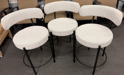 Set of three modern bar stools featuring textured white upholstered seats and curved backrests with sleek black metal frames and built-in footrests.