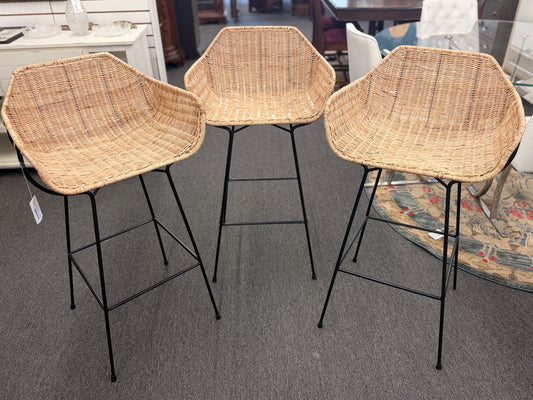 Set of three modern bar stools featuring woven rattan bucket-style seats, slim black iron frames, and built-in footrests.