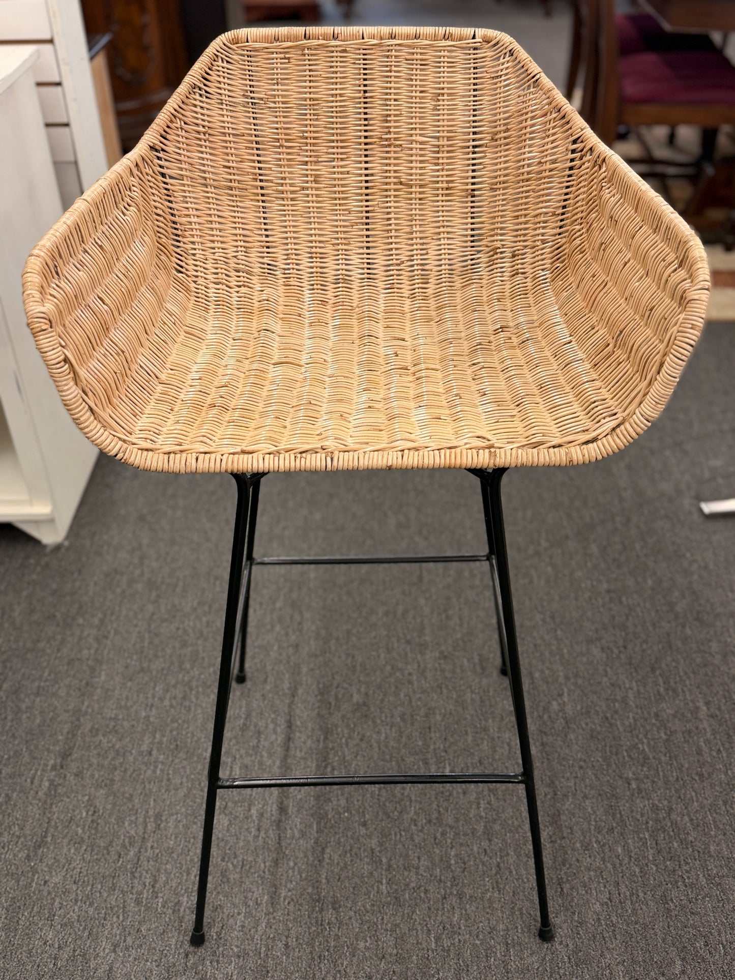 Set of three modern bar stools featuring woven rattan bucket-style seats, slim black iron frames, and built-in footrests.