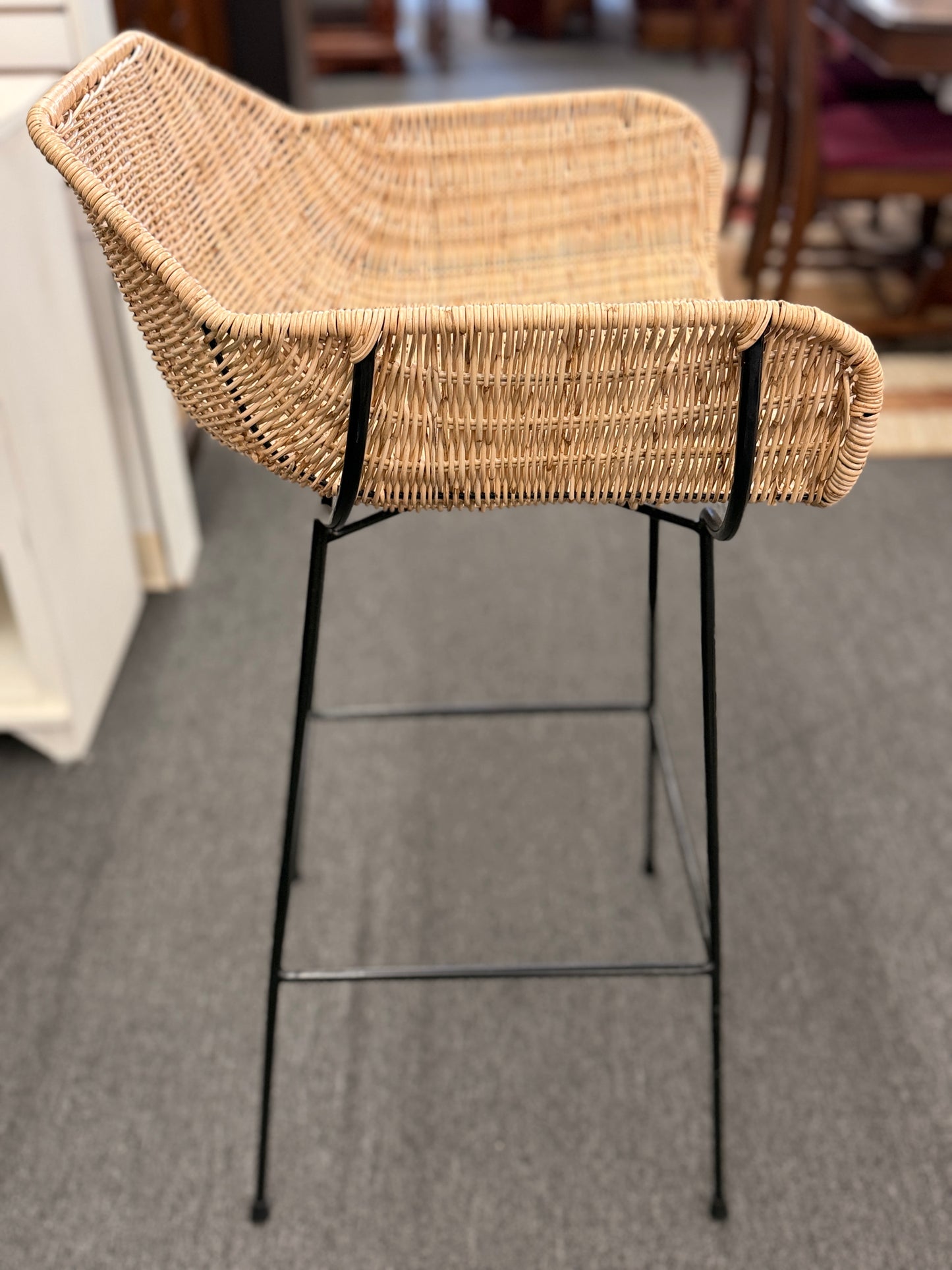Set of three modern bar stools featuring woven rattan bucket-style seats, slim black iron frames, and built-in footrests.