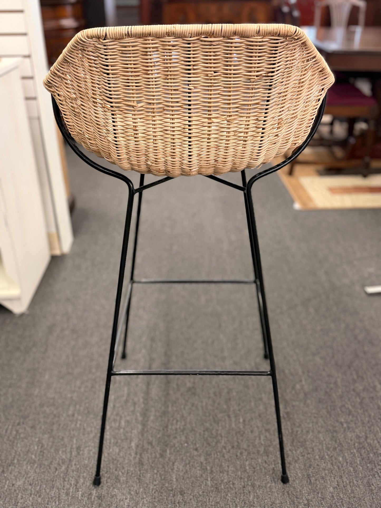 Set of three modern bar stools featuring woven rattan bucket-style seats, slim black iron frames, and built-in footrests.
