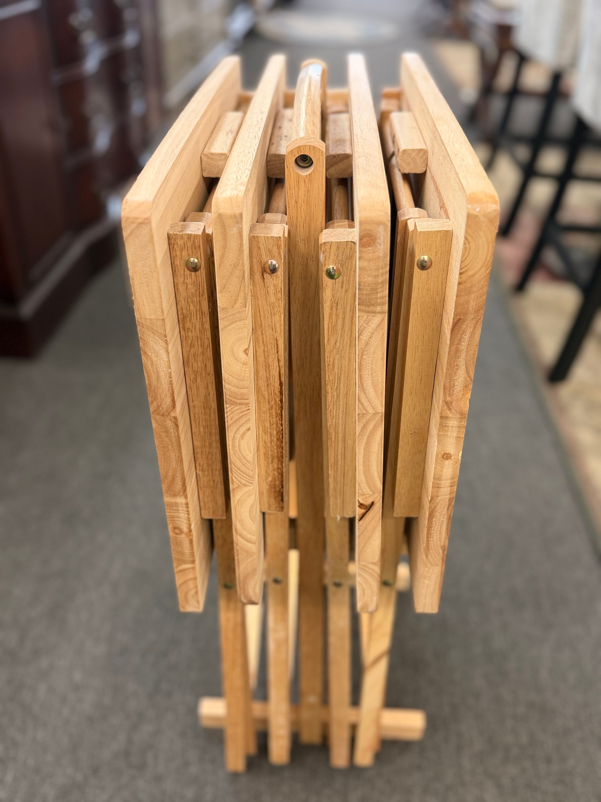 Set of four light wood folding TV tray tables stored on a matching wooden stand for compact, space-saving storage.