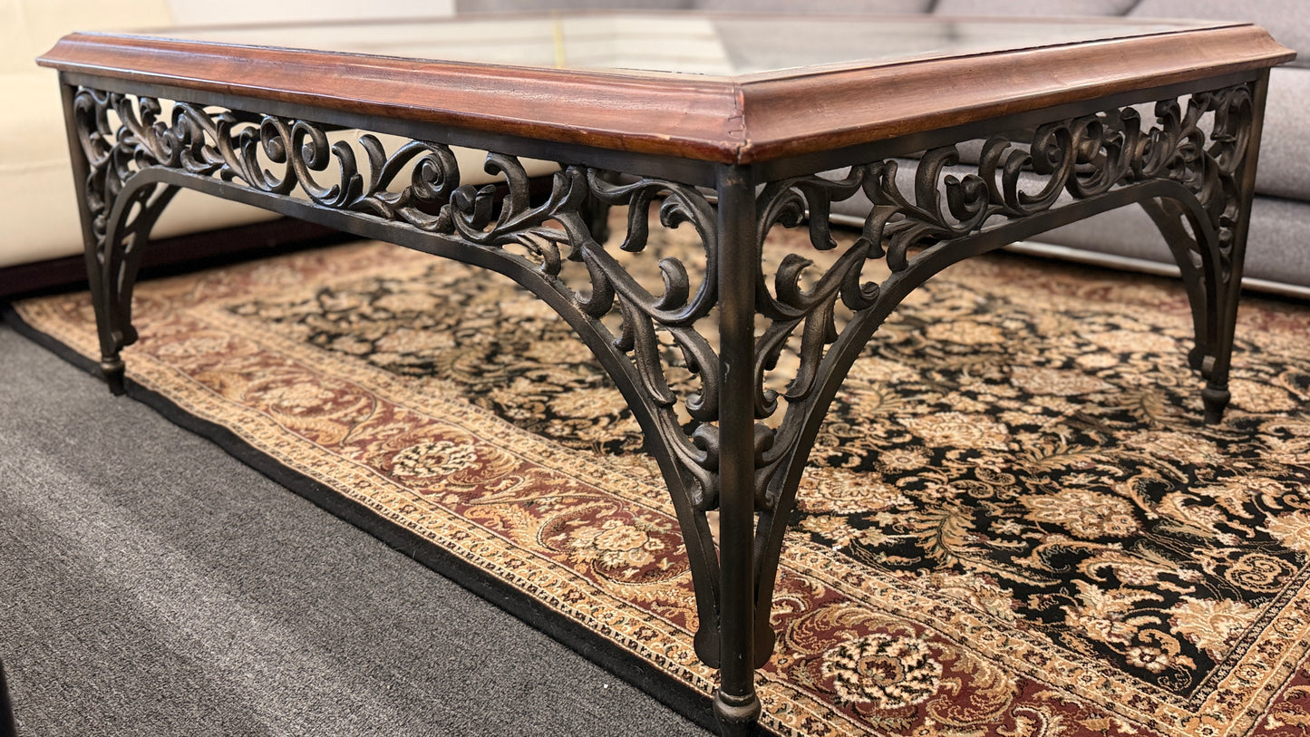 Square coffee table featuring a clear glass top insert, thick wooden frame, and an ornate scrolled metal base with traditional styling.