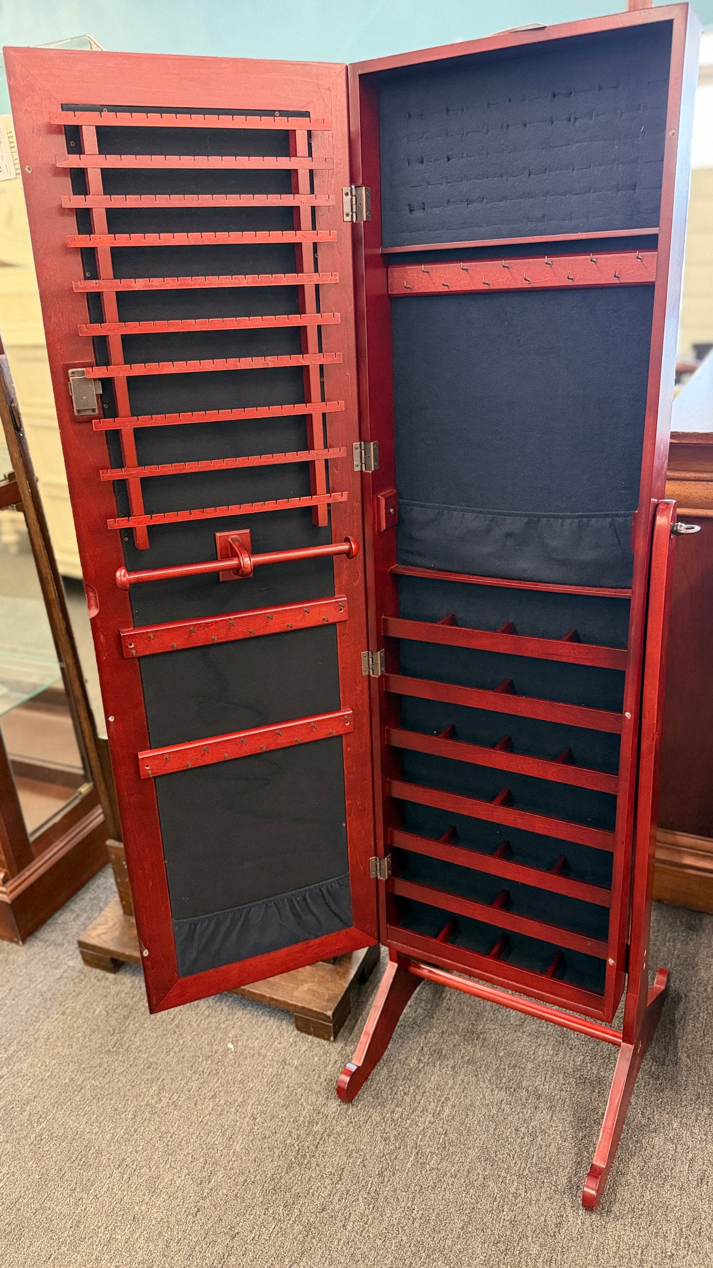 A full-length tilting floor mirror mounted in a wooden frame that opens into a locking internal jewelry armoire.