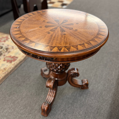 A round wooden pedestal side table featuring a geometric starburst inlay top, carved pineapple pedestal column, and tripod feet in good condition.