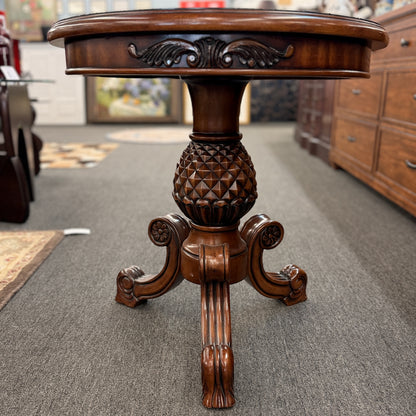 A round wooden pedestal side table featuring a geometric starburst inlay top, carved pineapple pedestal column, and tripod feet in good condition.
