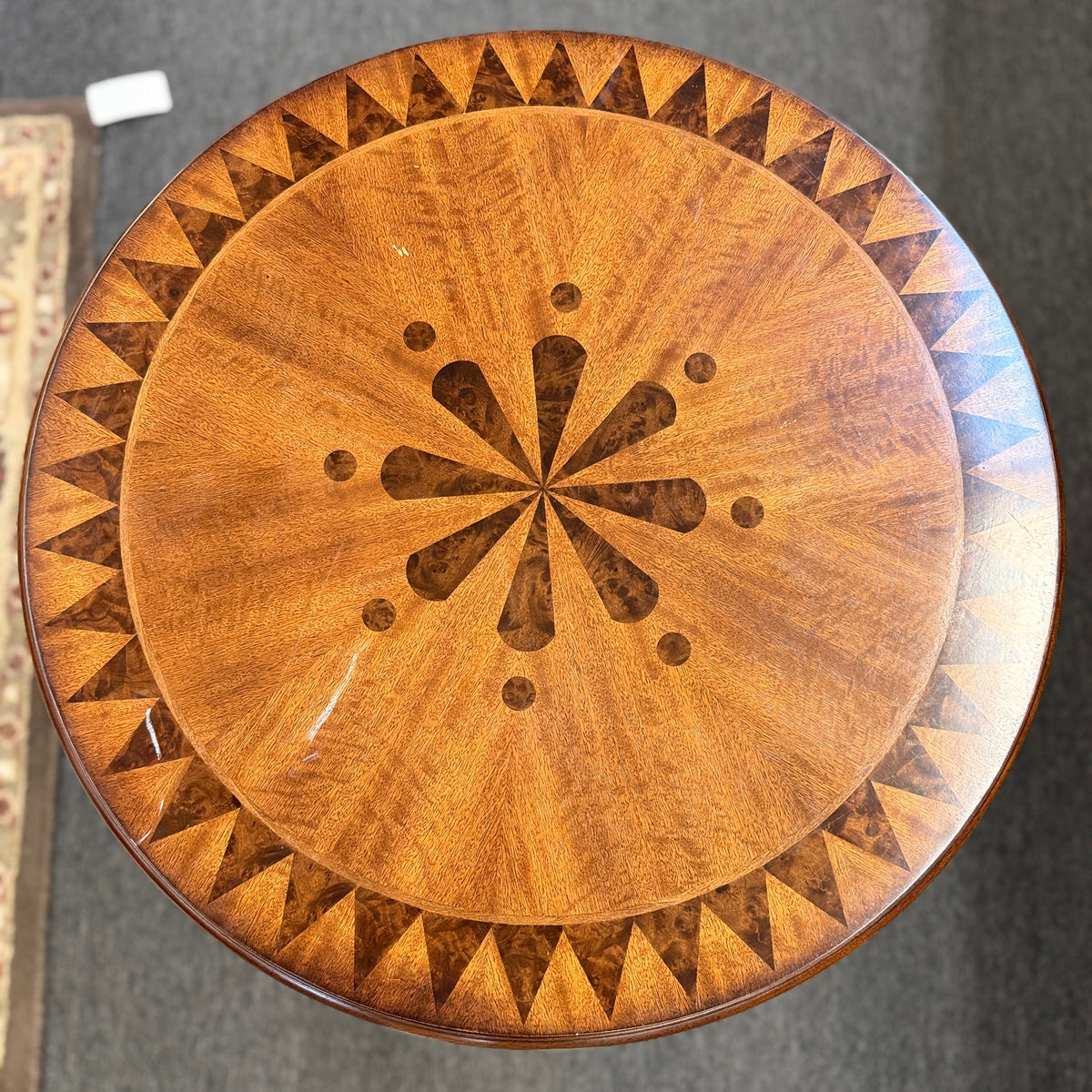 A round wooden pedestal side table featuring a geometric starburst inlay top, carved pineapple pedestal column, and tripod feet in good condition.