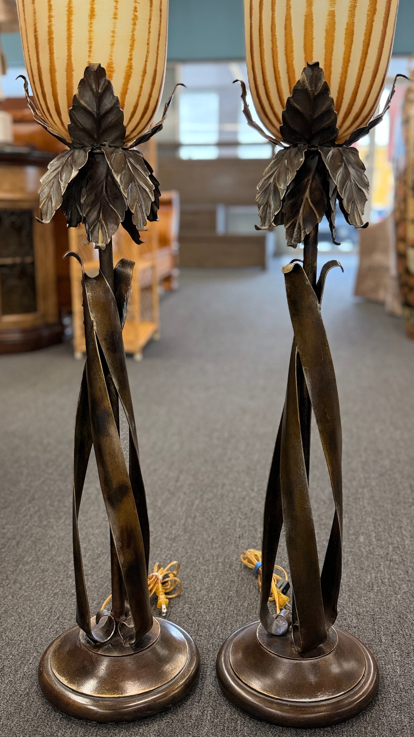 A pair of tall decorative table lamps featuring flared amber striped glass shades set in metal bases with sculpted leaves and twisted dark metal stems.