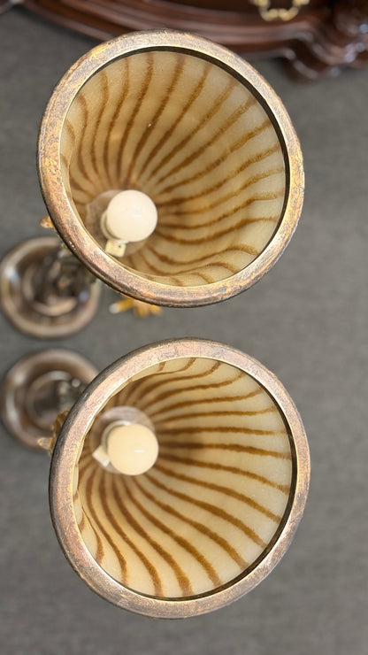 A pair of tall decorative table lamps featuring flared amber striped glass shades set in metal bases with sculpted leaves and twisted dark metal stems.