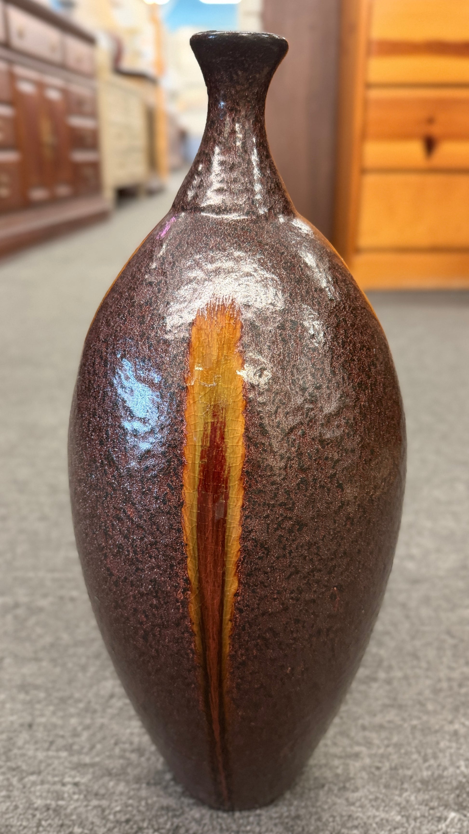 A tall teardrop-shaped ceramic vase featuring a textured mottled dark brown glaze with a vertical yellow and red-brown streak.