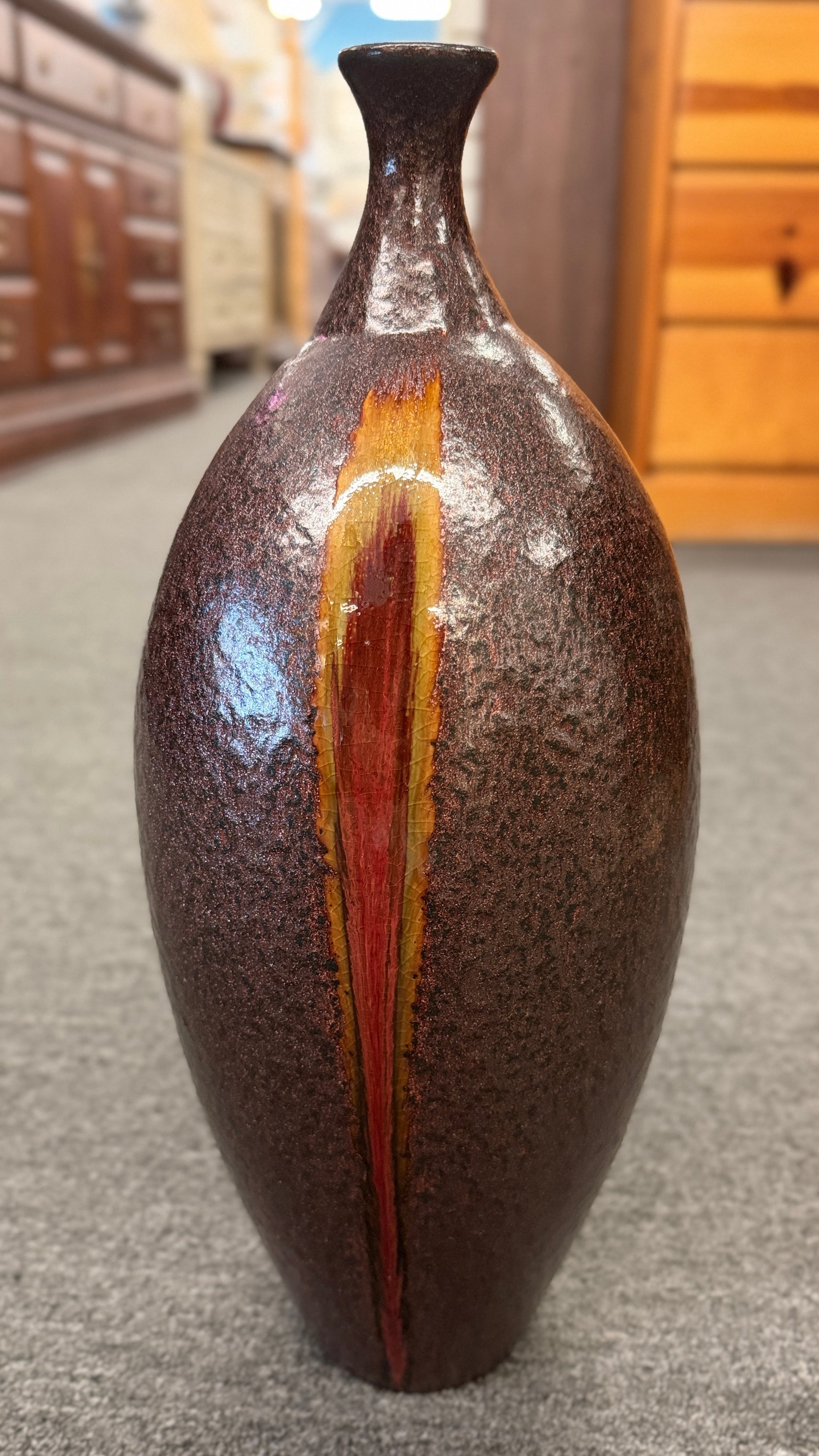 A tall teardrop-shaped ceramic vase featuring a textured mottled dark brown glaze with a vertical yellow and red-brown streak.