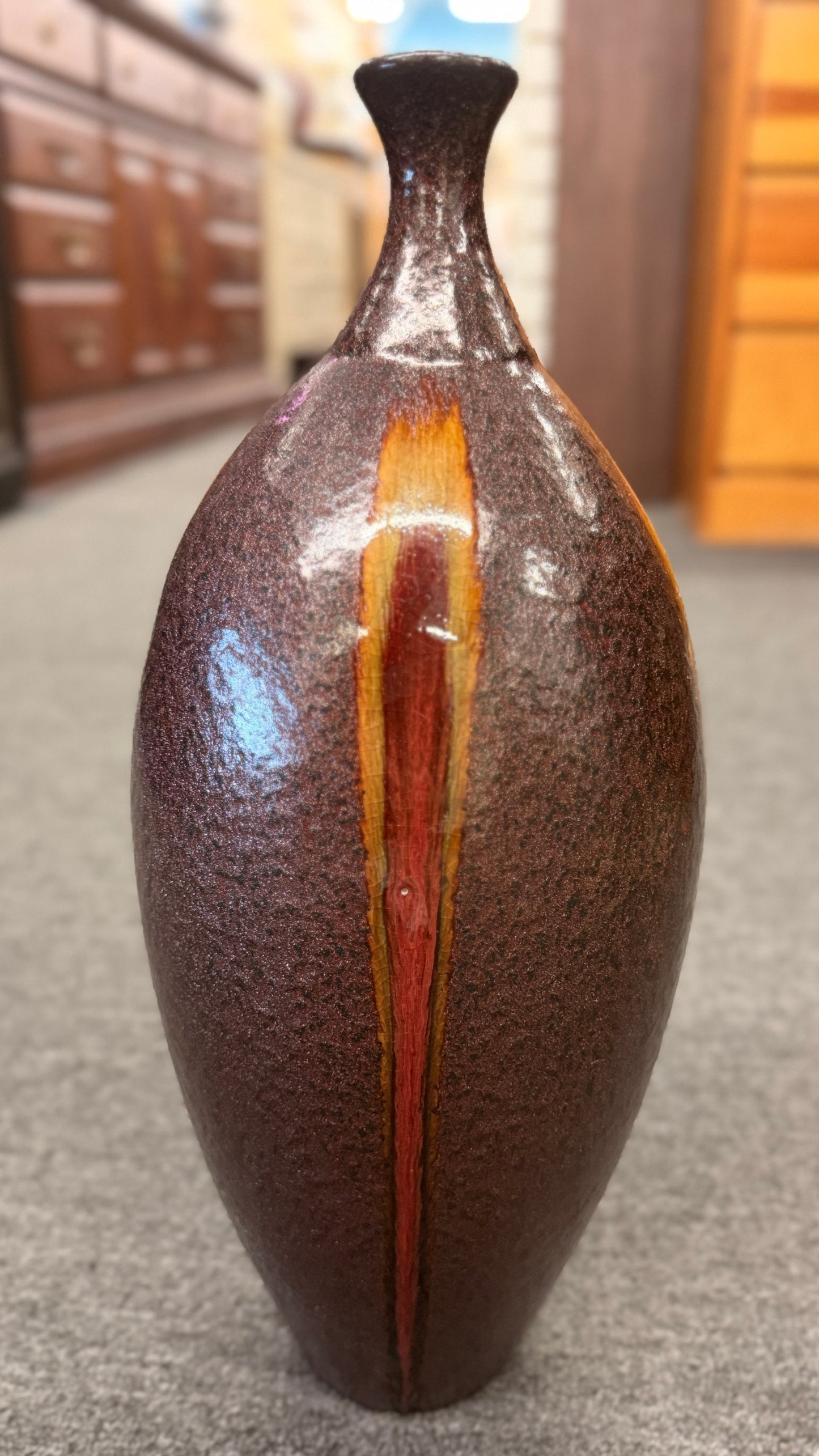 A tall teardrop-shaped ceramic vase featuring a textured mottled dark brown glaze with a vertical yellow and red-brown streak.