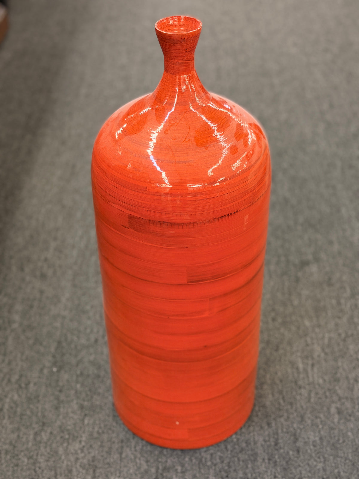 A tall slender ceramic floor vase with a narrow neck, vibrant glossy orange finish, and subtle horizontal ribbing in excellent condition.
