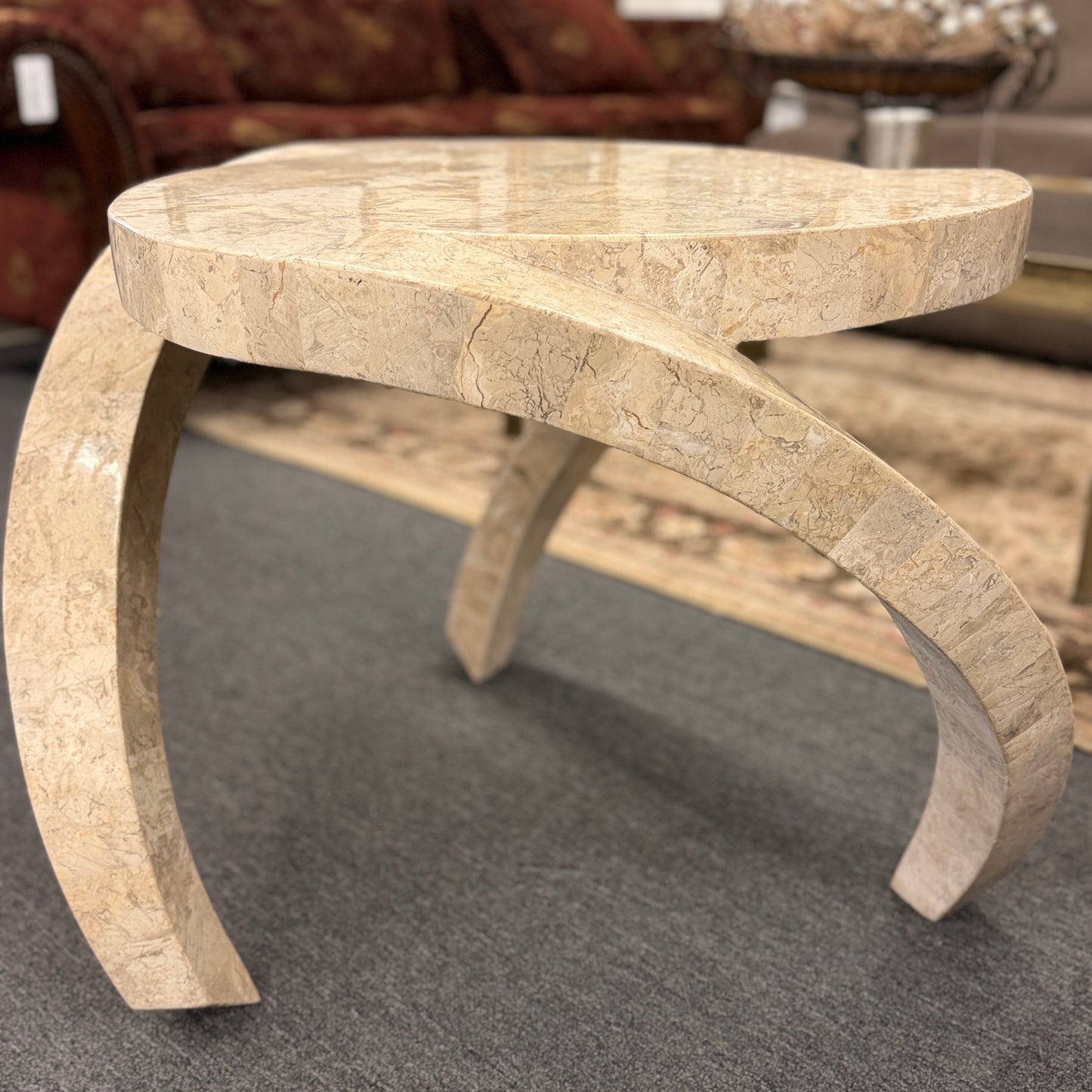 Tessellated stone end table featuring a polished light-colored stone mosaic, organic rounded triangular top, and sculptural curved three-leg base.