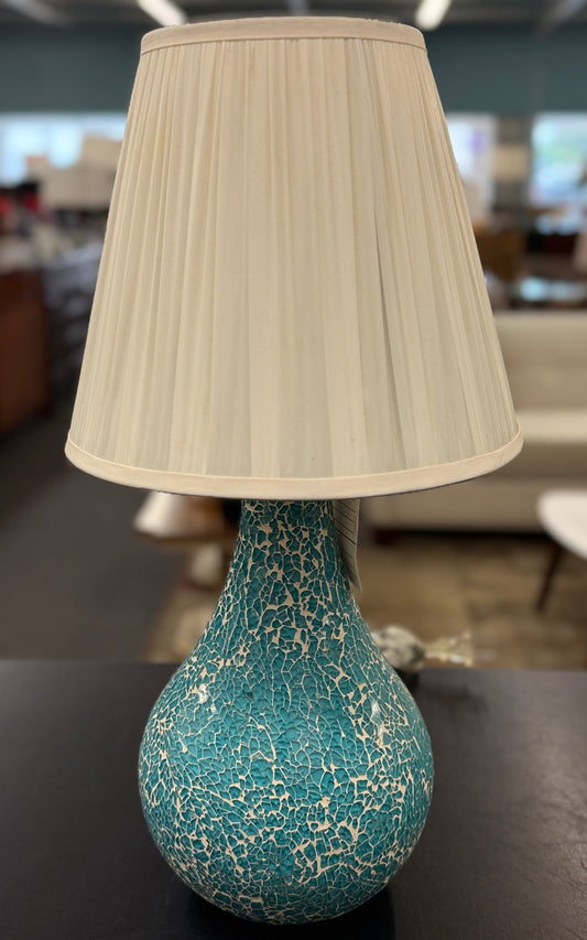 A teardrop-shaped ceramic table lamp with a textured teal and white crackle glaze base and a classic white pleated fabric lampshade.