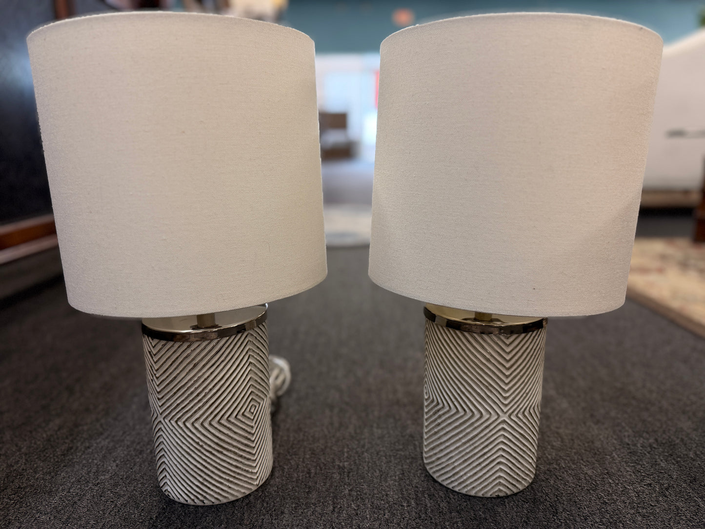 A pair of identical table lamps featuring textured white cylindrical ceramic bases with a geometric diamond pattern, white drum shades, and silver-toned hardware.