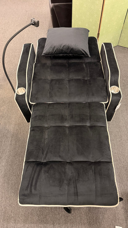 Plush theater-style sleeper chair upholstered in fabric with contrast piping, built-in cup holders, an adjustable reading light, and a matching throw pillow.