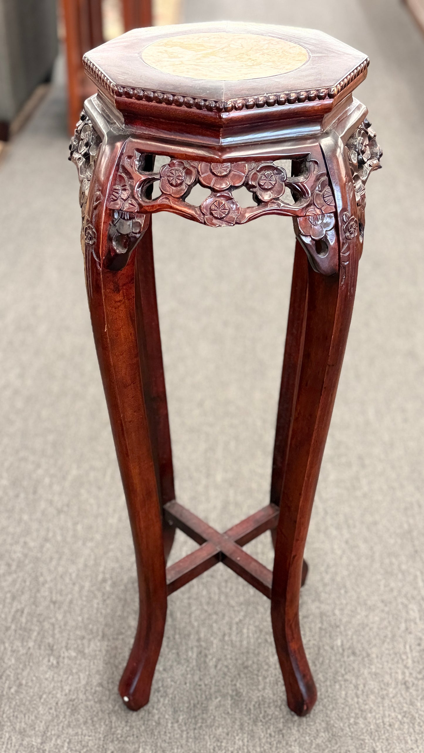 A traditional Asian-style tall dark wood plant stand featuring a hexagonal marble inset top, pierced floral apron, and curved legs with an X-stretcher base in good condition.