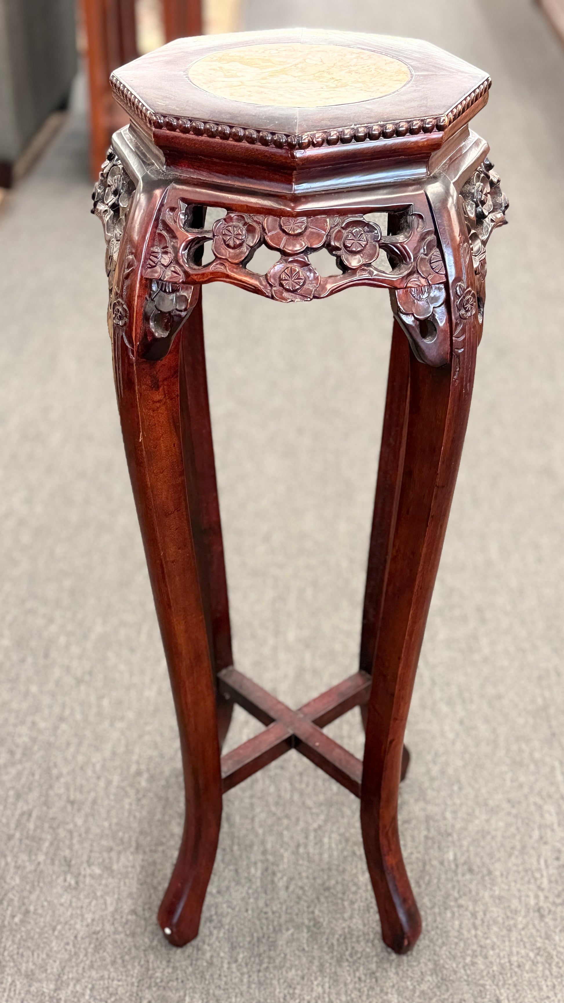 A traditional Asian-style tall dark wood plant stand featuring a hexagonal marble inset top, pierced floral apron, and curved legs with an X-stretcher base in good condition.