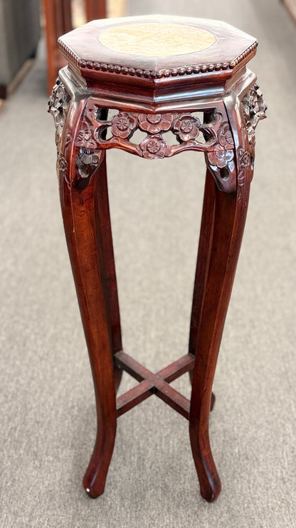 A traditional Asian-style tall dark wood plant stand featuring a hexagonal marble inset top, pierced floral apron, and curved legs with an X-stretcher base in good condition.