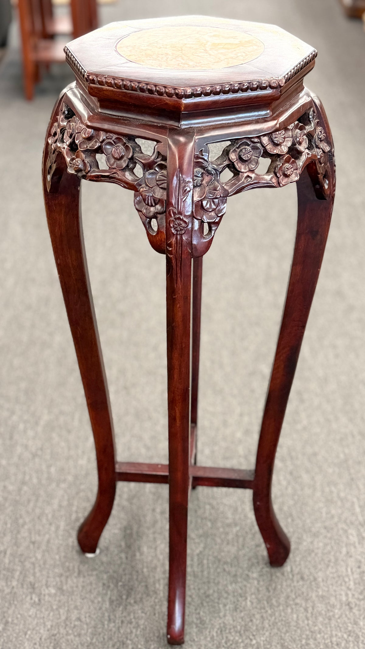 A traditional Asian-style tall dark wood plant stand featuring a hexagonal marble inset top, pierced floral apron, and curved legs with an X-stretcher base in good condition.