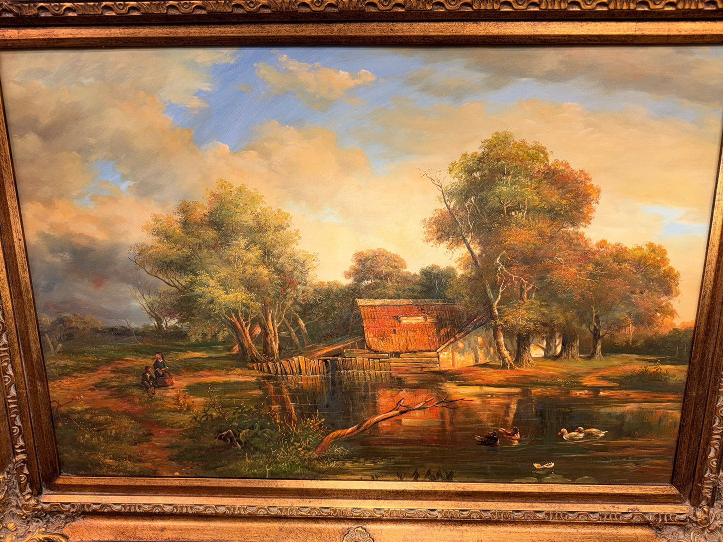 A traditional pastoral landscape painting depicting a lakeside cabin, autumn trees, and ducks in an ornate carved metallic-gold frame in excellent condition.