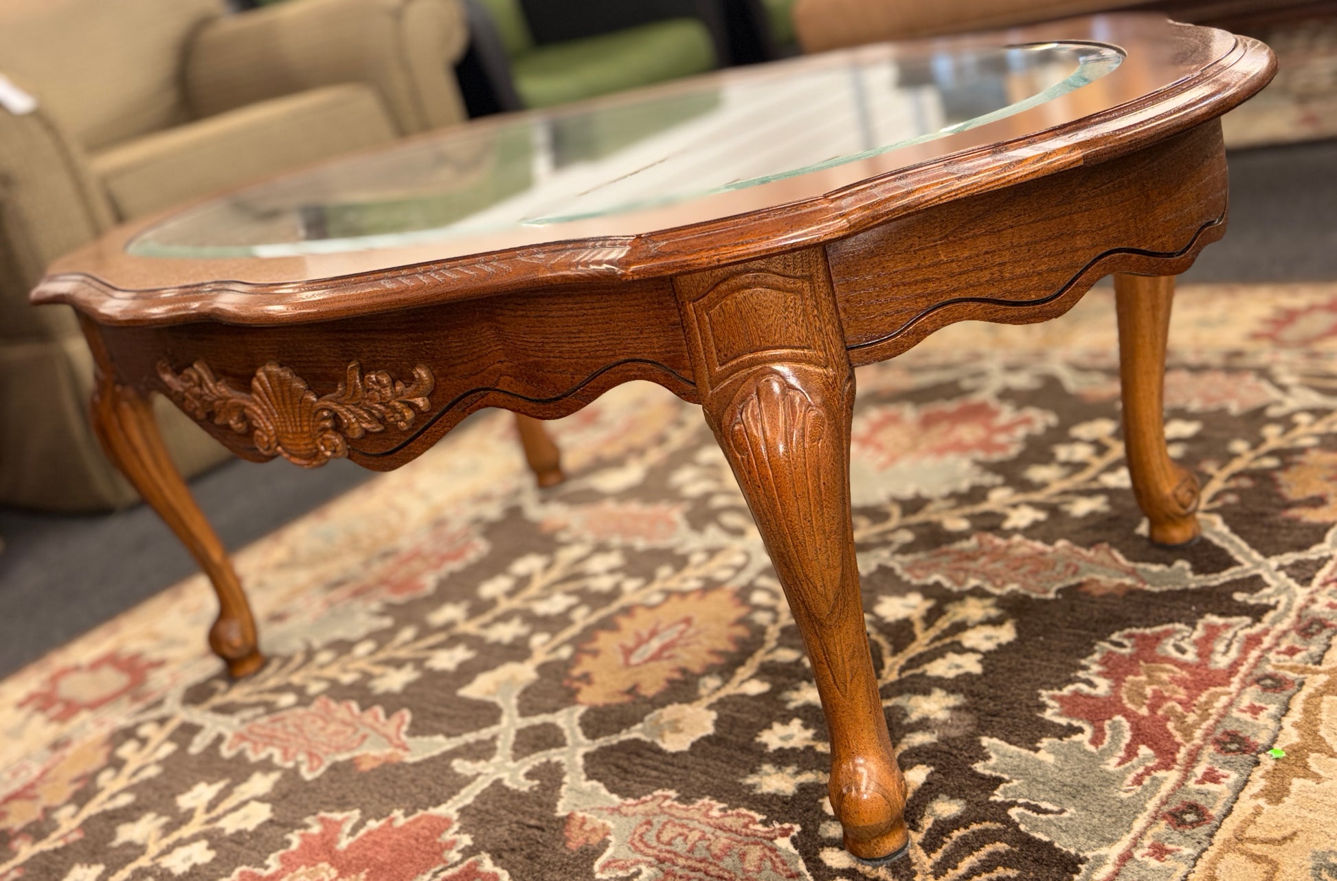 A classic oval coffee table featuring an inset clear glass top, hand-carved shell and floral details on the apron, and sweeping cabriole legs.