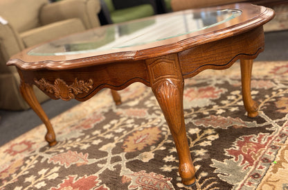 A classic oval coffee table featuring an inset clear glass top, hand-carved shell and floral details on the apron, and sweeping cabriole legs.