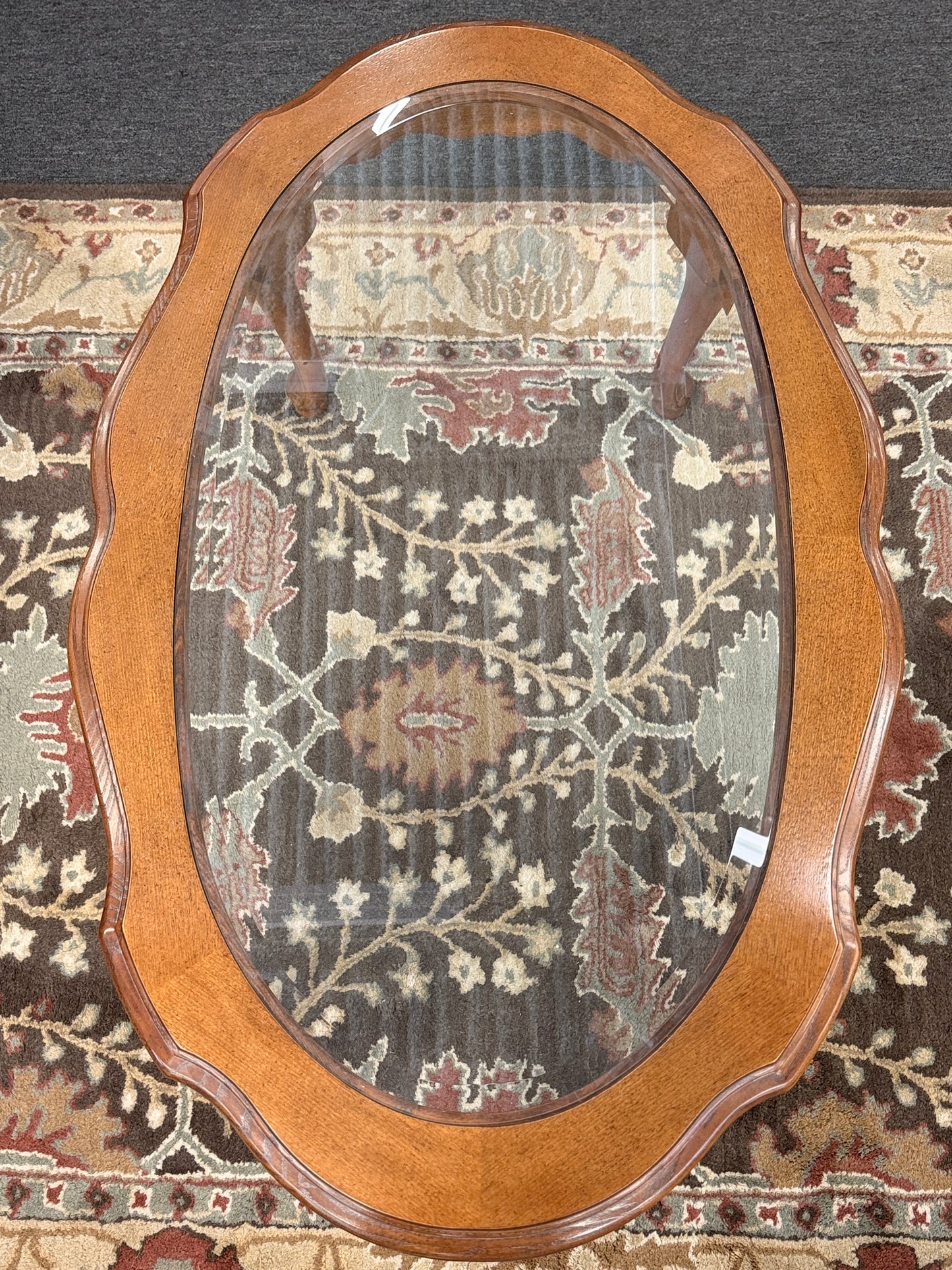 A classic oval coffee table featuring an inset clear glass top, hand-carved shell and floral details on the apron, and sweeping cabriole legs.