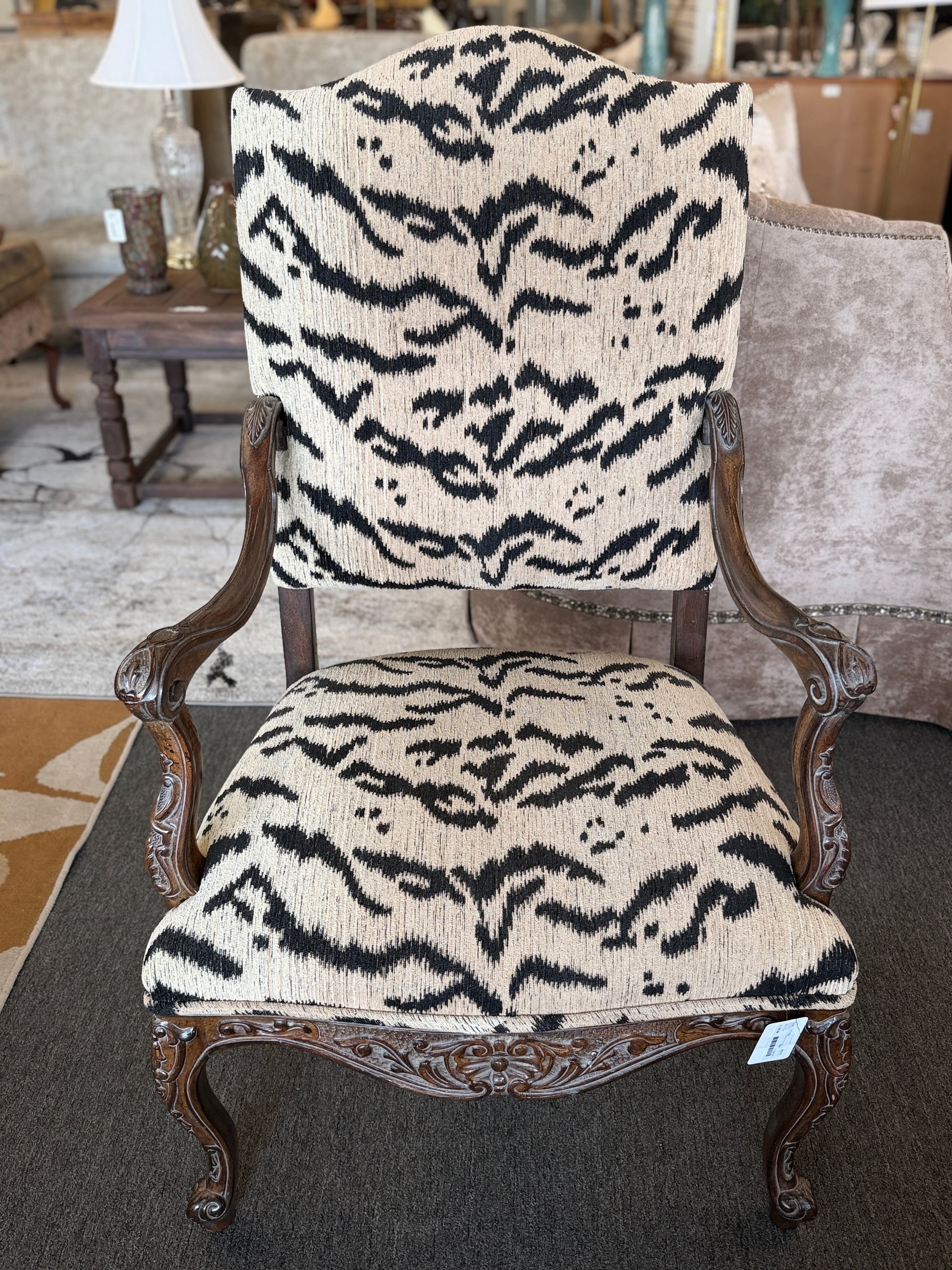 Traditional accent chair with an intricately carved dark wood frame, scrolled arms, cabriole legs, and black and cream animal-print upholstery.