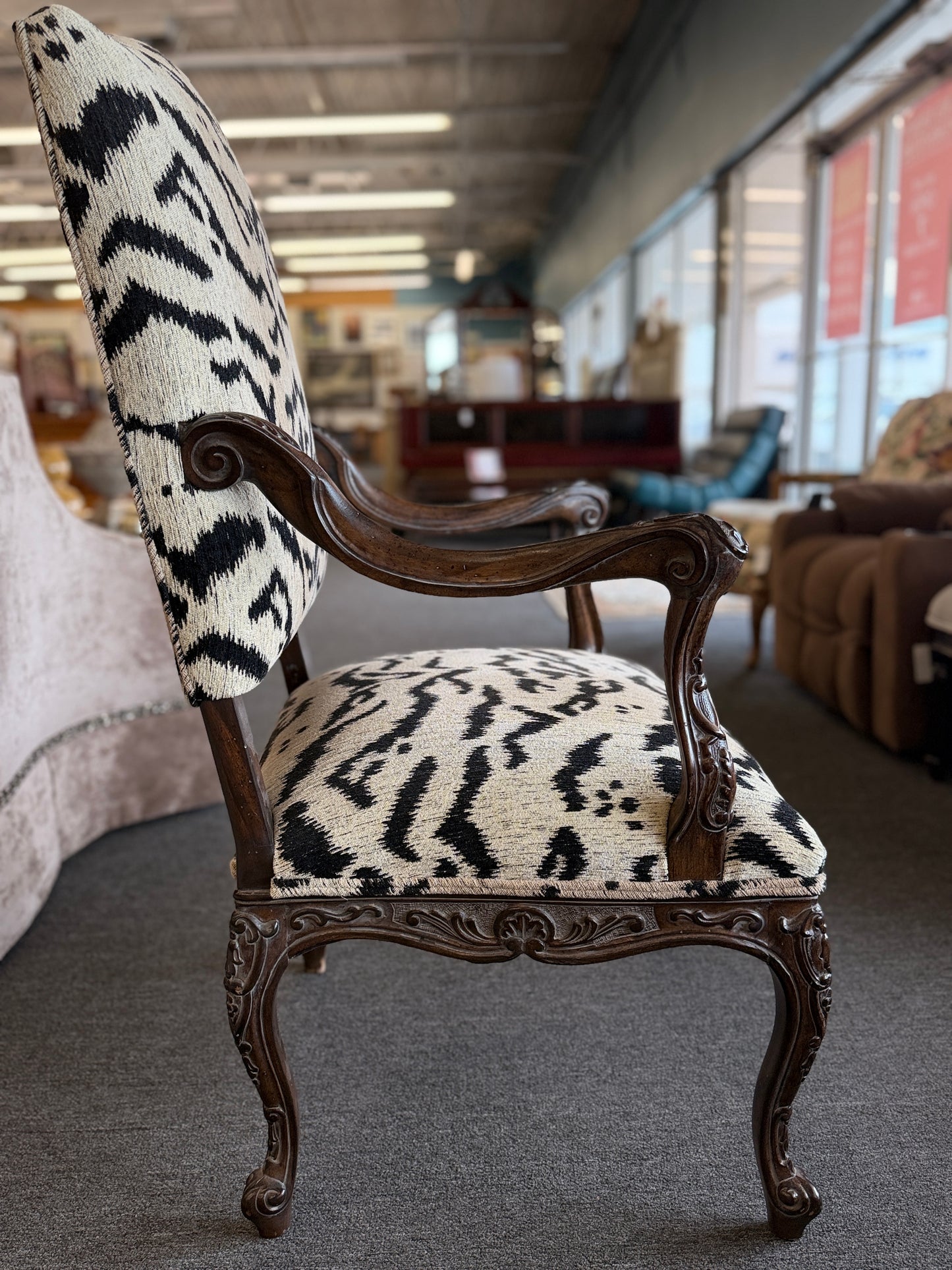 Traditional accent chair with an intricately carved dark wood frame, scrolled arms, cabriole legs, and black and cream animal-print upholstery.