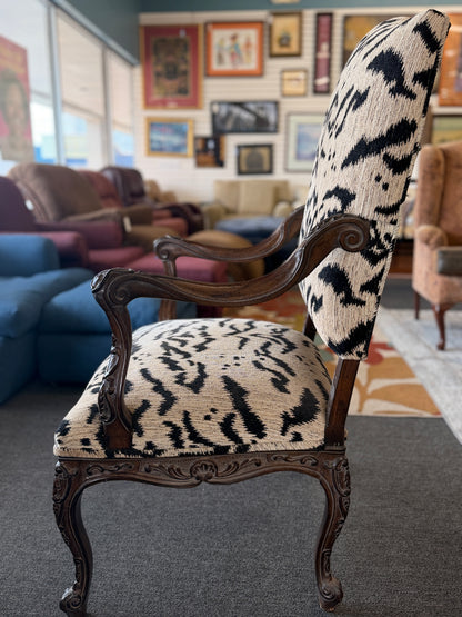 Traditional accent chair with an intricately carved dark wood frame, scrolled arms, cabriole legs, and black and cream animal-print upholstery.