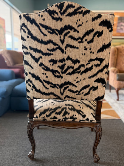 Traditional accent chair with an intricately carved dark wood frame, scrolled arms, cabriole legs, and black and cream animal-print upholstery.