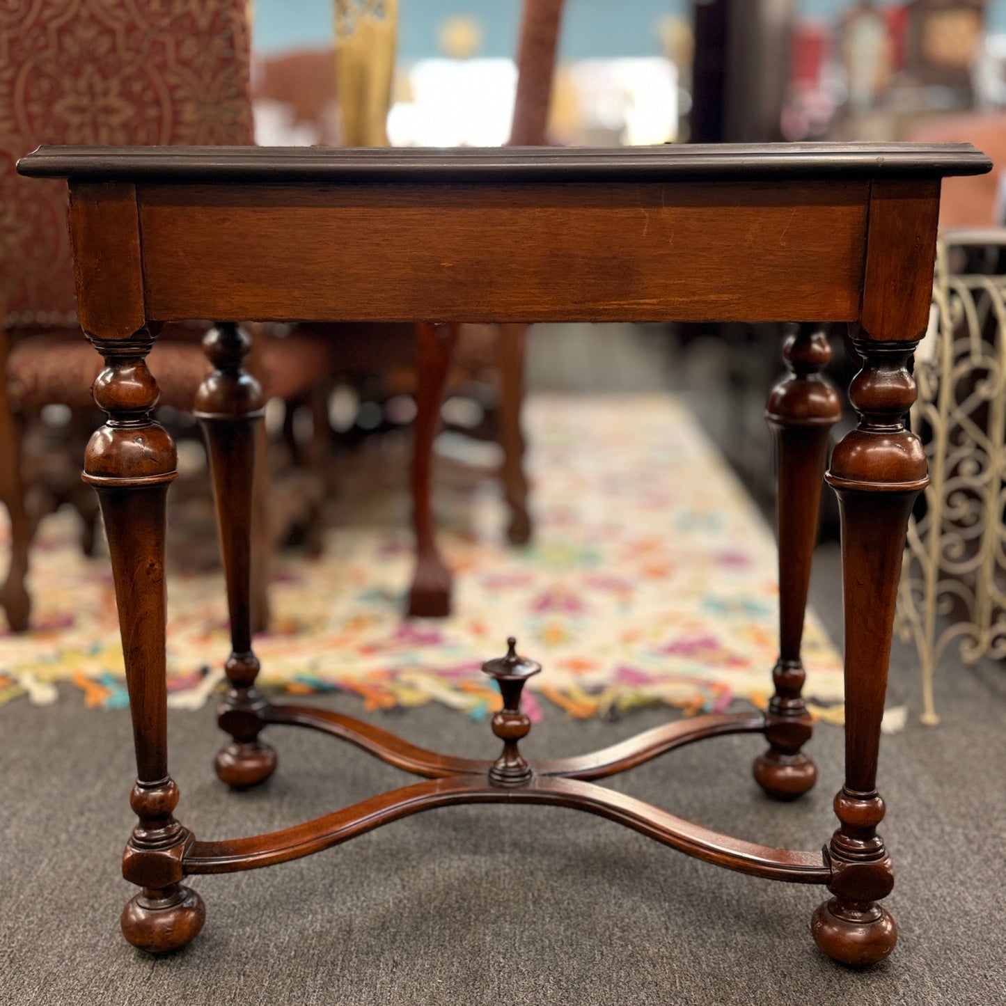Traditional carved wood console table featuring two front drawers, turned carved legs, an embossed tabletop with nailhead trim, and a curved cross-stretcher with a decorative center finial.
