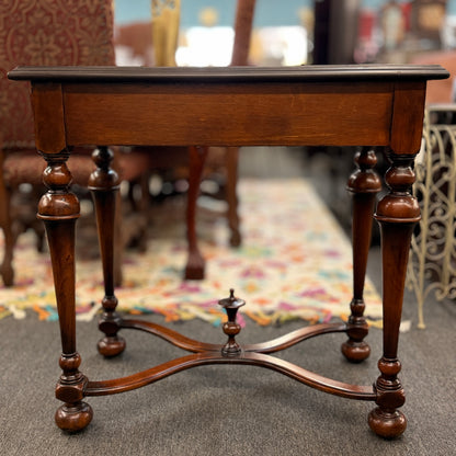 Traditional carved wood console table featuring two front drawers, turned carved legs, an embossed tabletop with nailhead trim, and a curved cross-stretcher with a decorative center finial.