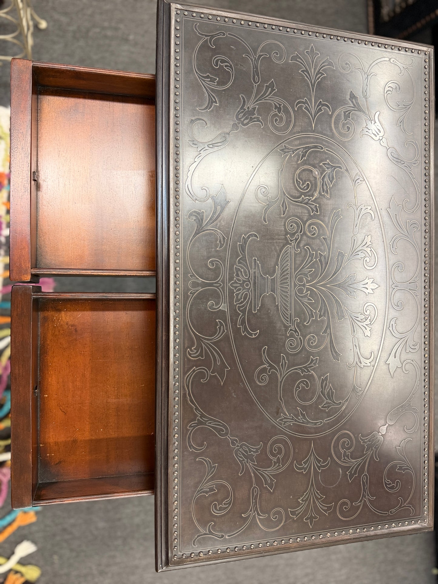 Traditional carved wood console table featuring two front drawers, turned carved legs, an embossed tabletop with nailhead trim, and a curved cross-stretcher with a decorative center finial.