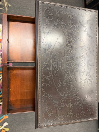 Traditional carved wood console table featuring two front drawers, turned carved legs, an embossed tabletop with nailhead trim, and a curved cross-stretcher with a decorative center finial.